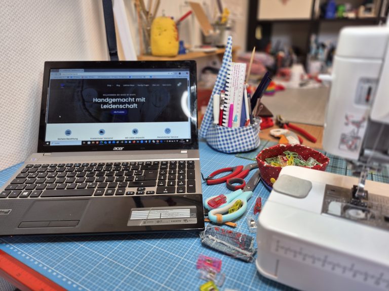 Nähtisch mit Nähmaschine, Stoffen, Nähzubehör und geöffnetem Laptop mit Website – zeigt kreatives Arbeiten im Handmade-Business