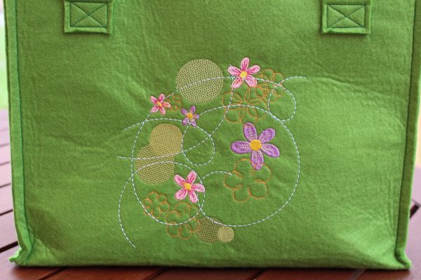 Großaufnahme vom Mandala-Blumenmotiv in Rosa und Lila auf hellgrünem Filz